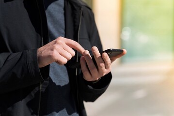 Close-up of the hands of a caucasian young man in casual clothes using a mobile phone while walking outdoors on a warm spring day. Lifestyle, Technology, Work, Freelancing