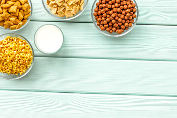 Various corn cereals in bowls and milk on mint wooden background top view copyspace