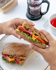 Hands holding half of a fresh sandwich filled with colorful vegetables and meat.