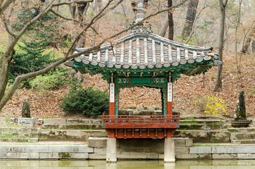 A small gazebo sits in a park with a pond in the background