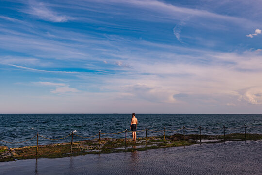 Boy standing on edge of the Bogey Hole rock pool looking out at the ocean