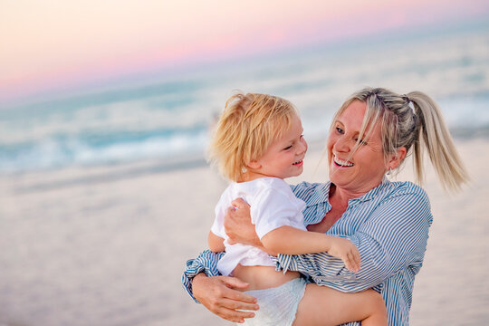 Mother carrying son on the beach in pink twilight light. Sunset on the Gold Coast.