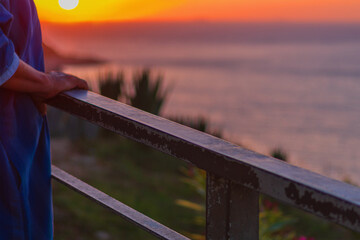 Handrail on which an elderly unrecognizable man leans with his hands stands against the background of an amazing sunset over the sea horizon, enjoying the magnificent landscape, view and life