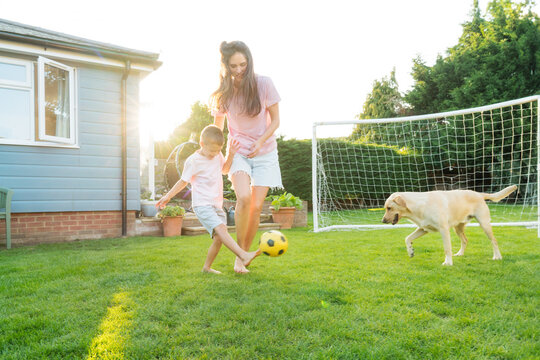 Young mother and son plays soccer with dog and have fun together. Happy family playing football with pet. Fun Playing Games in Backyard Lawn on Sunny Summer Day. Motherhood, childhood, togetherness