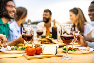 Young people enjoying delicious barbecue dinner party drinking red wine - Multiracial family having diner time together outside - Happy friends eating fresh food sitting at restaurant table - 779851611