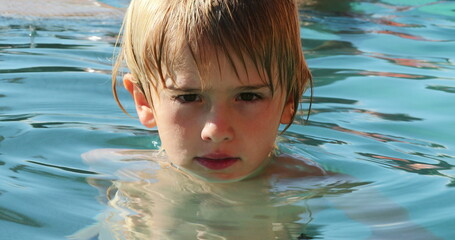 Young boy inside swimming pool water looking to camera