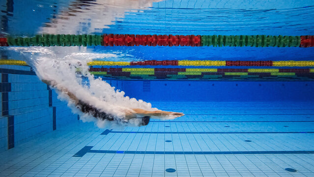 Female swimmer in water immersion phase, entering and sliding below the water surface making wonderful bubbles, underwater shot.