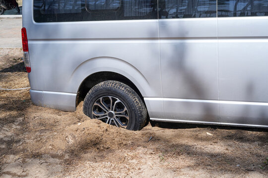 The wheel of a silver van stuck in the sand, Stuck tires, Car bogged into lava sandy. Accident occurred during driving on sandy beach.