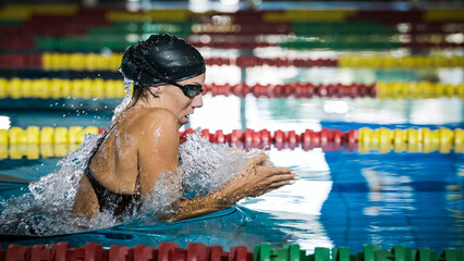 Female athlete swimming in breaststroke style in the pool lane, stroking, immersing, and lifting...