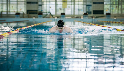 Professional male swimmer performing butterfly style in the indoor lap pool lane, front view....