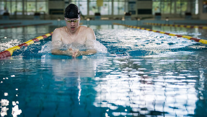 Front view of a male athlete swimming breaststroke style in the pool between two swimming lane...