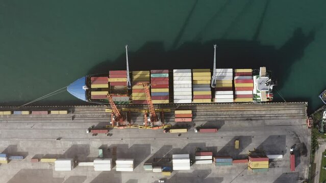 Top down aerial view of cargo ship loading containers. Showcases maritime shipping efficiency. Part of global distribution network.