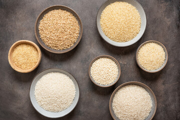 Collection of various dry rice in bowls on a dark rustic background. Top view, flat lay.