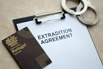 Passport of Portugal and Extradition Agreement with handcuffs on table close up