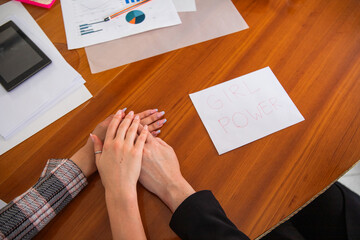 Businesswomen make a stack with their hands near a paper with 