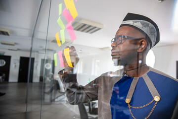 An African businessman writes on colorful sticky notes hanging on the wall in the office