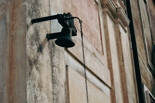Antica campana in bronzo scuro montata sulla facciata storica di una chiesa o palazzo d'epoca con catena in ferro e intonaco antico rovinato dal tempo