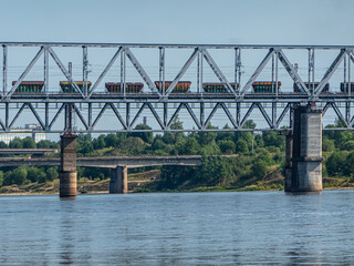 Railway metal bridge over the river. A freight train with wagons for fertilizers is moving along the bridge.