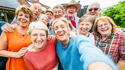 Happy group of senior people smiling at camera outdoors - Older friends taking selfie pic with smart mobile phone device - Life style concept with pensioners having fun together on summer holiday - 779873209