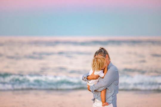 Mother and toddler son embracing on the beach with pink sunset sky