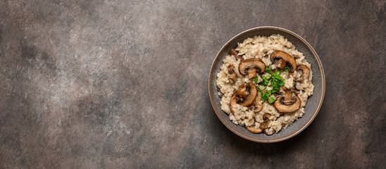 Risotto with brown champignons mushrooms on a dark grunge background, banner. View from above, copy space