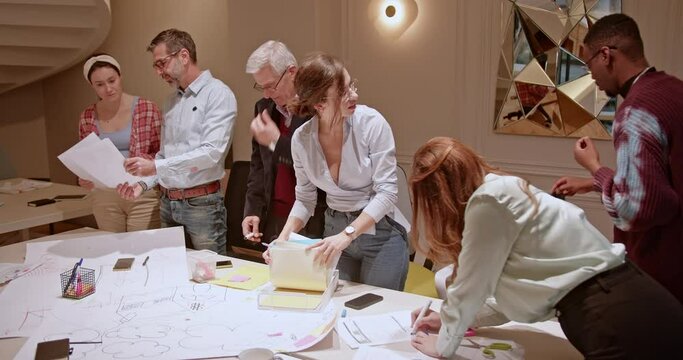 In a office, a group of multiethnic business employees is engaged in a discussion over project materials at a cluttered table, showcasing their collaborative efforts and dedication to their work.