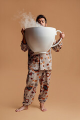 A sleepy man in pajamas drinks a giant cup of coffee to wake up