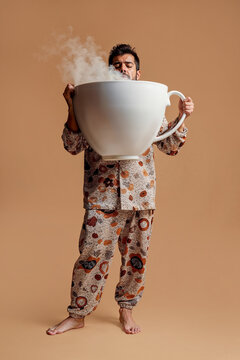 A sleepy man in pajamas drinks a giant cup of coffee to wake up