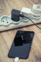 Black smartphone and chargers connected to electrical power strip. Various devices charging concept