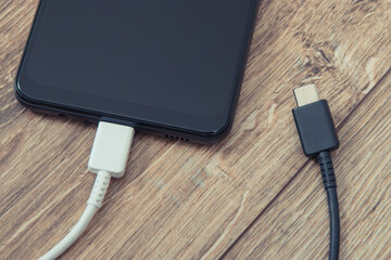 Black smartphone with charger cables on wooden background. Telephone charging concept