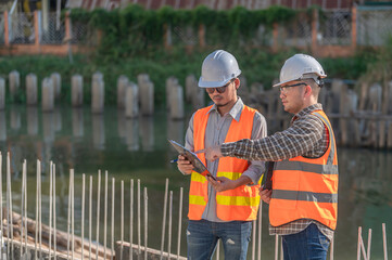 Construction engineer working on a bridge construction site over a river,Civil engineer supervising work,Foreman inspects work at a construction site,Discuss technical problems together - obrazy, fototapety, plakaty