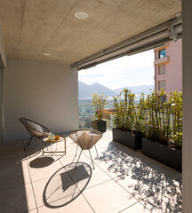 Large terrace of a house in Switzerland with a view of Lake Maggiore. Sunny day and two cosy armchairs with cushion.
