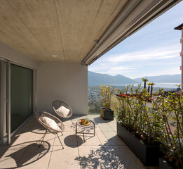 Large terrace of a house in Switzerland with a view of Lake Maggiore. Sunny day and two cosy armchairs with cushion. - 779879038