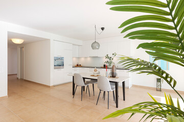 Large modern white kitchen with a marble table and four chairs in front. This is the interior of a...