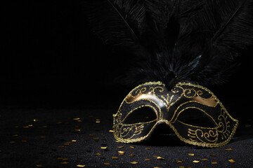 Carnival gold mask with feathers and confetties on black background.