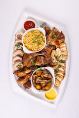 Top view Assorted roasted meats, colorful vegetables, and golden potatoes garnished with fresh parsley and savory sauces on a white platter
