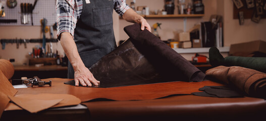 Cobbler working with skin textile in workshop. Tailor hold different rolls natural brown leather