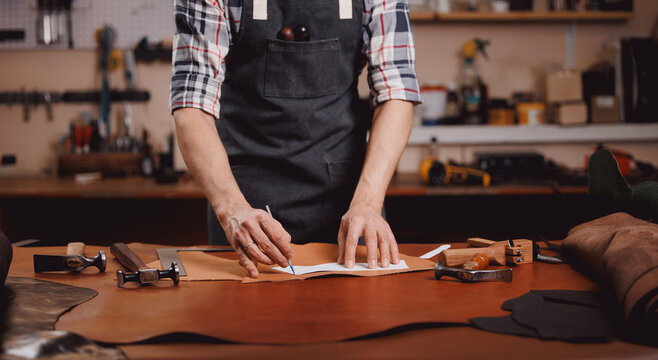 Cobbler Man tailor chooses roll of brown leather for sewing a bag or shoes made of skin in workshop. Banner of industry leather products
