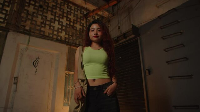 Low angle portrait of gen Z Asian girl in crop top and jeans smiling at camera on empty stairwell