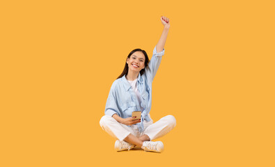 Excited woman making victory gesture on yellow background