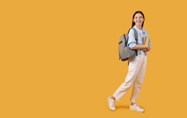 Fototapeta na wymiar Woman walking with backpack and books on yellow background