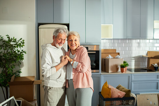 Senior couple holding hands and smiling in a new home with moving boxes - Powered by Adobe