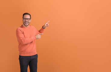 Portrait of male promoter laughing and pointing at copy space while marketing on orange background