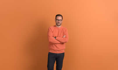Portrait of handsome young businessman in eyeglasses with arms crossed posing on orange background