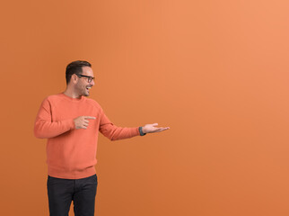Ecstatic salesman pointing at empty palm and demonstrating new product on isolated orange background