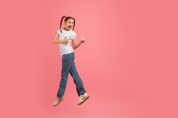 Energetic girl jumping and pointing on pink