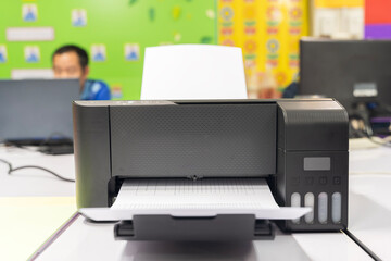 A black printer is open and has a white sheet of paper inside.