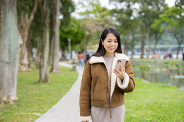 Woman walk along the park with mobile phone