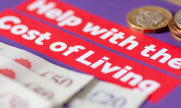 A macro close up of a government leaflet of help with the cost of living with bank notes and coins. A cost of living and poverty concept.