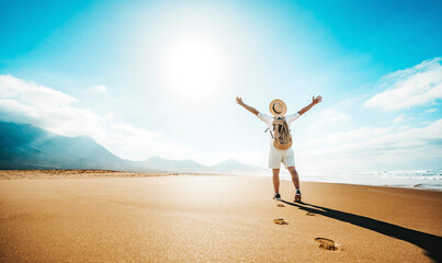 Happy traveler with hands up standing at the beach - Delightful man enjoying success and freedom outdoors - Wanderlust, wellbeing, travel and summertime holidays concept - 779900621